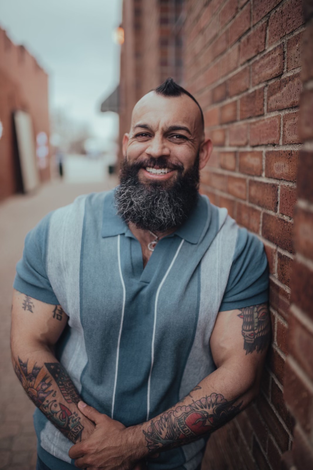 A man with a beard and mustache standing next to a brick wall.